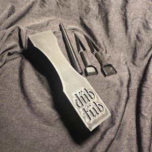 May include: A black, rectangular, 3D printed box with the words "Wild Thing" embossed on the side. The box contains four black tools, including a long, thin, pointed tool and three shorter, flat tools.