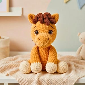 May include: A handmade, plush crochet horse in shades of orange and brown. The horse has a detailed mane, large, expressive eyes, and white hooves. It is sitting on a cream-colored blanket.