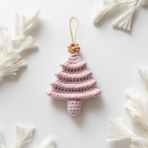 Peut inclure: Une décoration de Noël en forme de sapin de Noël en crochet rose avec une étoile brune sur le dessus. L'ornement est suspendu à une ficelle dorée.