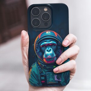 May include: A black phone case with a colorful illustration of a monkey wearing an astronaut helmet. The monkey is wearing a blue and green spacesuit with a black strap. The background is a dark blue with white stars.
