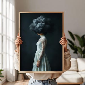 May include: A framed rectangular wall art print featuring a side profile of a figure wearing a light blue long-sleeved lace dress. The figure's head is replaced by a large, dark, textured storm cloud against a deep navy blue background.