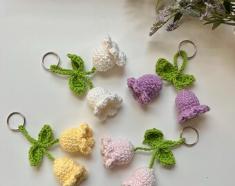 May include: Six crocheted flower keychains in different colors, including white, purple, yellow, and pink. Each keychain features a flower with a green stem and leaves.