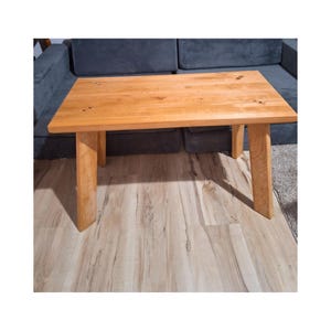 Peut inclure: Une table basse en bois de couleur brun clair avec un plateau rectangulaire et quatre pieds. La table est en bois massif et a une finition naturelle.