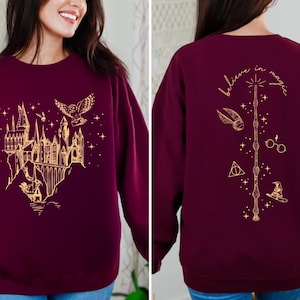 May include: A maroon sweatshirt with a gold graphic of Hogwarts castle on the front and the text "Believe in magic" with a wand and other Harry Potter symbols on the back.