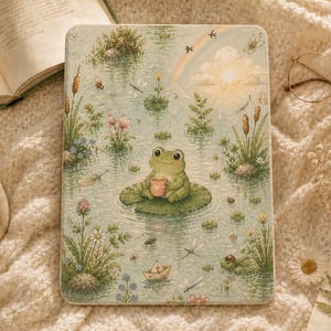 May include: A rectangular e-reader case featuring a detailed illustration of a green frog sitting on a lily pad in a pond. The scene includes cattails, dragonflies, a small paper boat, a rainbow, and a sun, all rendered in soft pastel tones.