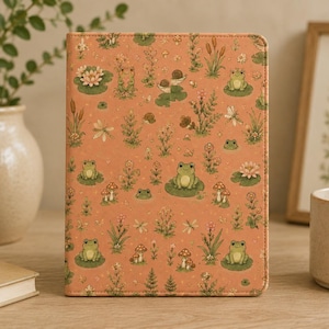 May include: A rectangular tablet case with a muted orange background featuring a repeating pattern of green frogs, brown snails, red and white mushrooms, pink water lilies, dragonflies, and various green plants and small flowers.