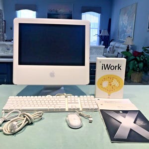 May include: A white Apple iMac desktop computer with a matching white keyboard and wired mouse. Included are an iWork software box and a Mac OS X Tiger manual. The computer features a large screen with a silver Apple logo on the front bezel.
