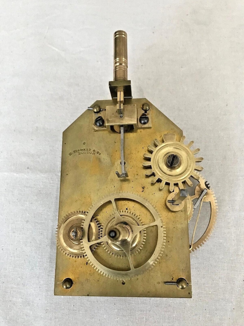 Puede incluir: Un movimiento de reloj de lat&oacute;n con una placa de lat&oacute;n y varios engranajes. La placa est&aacute; inscrita con "E. Howard & Co. Boston".