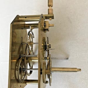 Puede incluir: Un mecanismo de relojer&iacute;a de lat&oacute;n con varios engranajes y una llave de cuerda. El mecanismo est&aacute; montado en una placa de lat&oacute;n con cuatro pilares de lat&oacute;n.