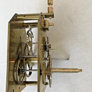 Puede incluir: Un mecanismo de reloj de lat&oacute;n con varios engranajes y una llave de cuerda. El mecanismo est&aacute; montado en una placa de lat&oacute;n y tiene una varilla de lat&oacute;n que se extiende desde el lateral.