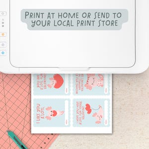 Puede incluir: Cuatro tarjetas de San Valent&iacute;n imprimibles con un ajolote con un globo en forma de coraz&oacute;n. Las tarjetas tienen un fondo azul y el texto "I like you a'lotl", "You are a'lotl fun Valentine", "I hope you have a'lotl fun today, Valentine!" y "Wishing you a happiness the Valentine's Day". Las tarjetas se est&aacute;n imprimiendo en una impresora blanca.