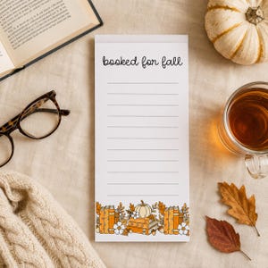 May include: A white rectangular notepad with the text booked for fall printed at the top. The notepad features horizontal lines for writing and a decorative border at the bottom showing orange books, a white pumpkin, and autumn leaves.