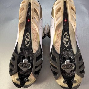 May include: Pair of white and black cycling shoes with a Specialized logo. The soles are visible, showing the cleat attachment points and the word "SPECIALIZED" in red. The shoes have a worn appearance.