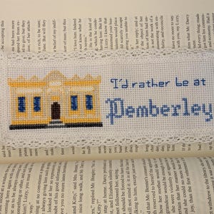May include: Embroidered bookmark with the text "I'd rather be at Pemberley" in blue thread. The bookmark features a cross-stitched image of a yellow building with blue windows and a white lace border.