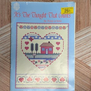 May include: A cross-stitch pattern book titled "It's The Thought That Counts" with a heart-shaped design featuring a house, trees, and hearts. The cover is light blue with text in red and the design in various colors.