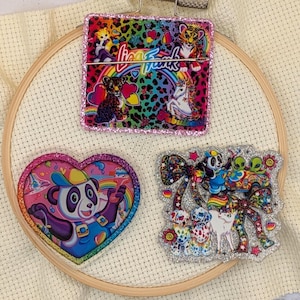May include: Three Lisa Frank acrylic pieces with glitter borders. The top rectangular piece features a tiger, leopard, and unicorn on a rainbow leopard print background. The heart-shaped piece shows a panda, and the third piece features a panda and dogs.
