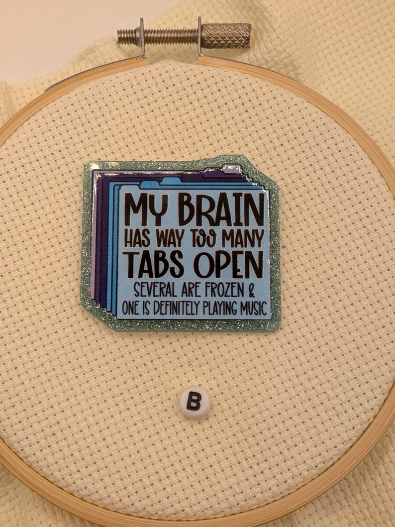 Peut inclure: Un cercle &agrave; broder avec un carr&eacute; bleu et scintillant portant le texte "MY BRAIN HAS WAY TOO MANY TABS OPEN. SEVERAL ARE FROZEN & ONE IS DEFINITELY PLAYING MUSIC." Une petite perle blanche avec la lettre "B" est &eacute;galement pr&eacute;sente.