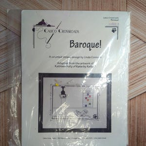 May include: A cross-stitch kit titled "Baroque!" by Calico Crossroads. The design, adapted from Kathleen Kelly's artwork, features a black cat on a pedestal, a stained-glass window, and a sleeping dog. The kit is sealed in plastic.