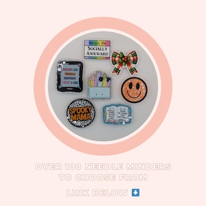K&ouml;nnte beinhalten: Eine Sammlung dekorativer Nadelhalter mit verschiedenen Designs, darunter ein Smiley, eine Schleife und Texte wie "Hello, I'm Socially Awkward" und "Spooky Mama". Die Nadelhalter sind auf einer wei&szlig;en Oberfl&auml;che angeordnet.
