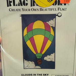 May include: A flag factory pattern with a colorful hot air balloon design. The balloon is yellow, pink, and green against a dark blue background. The text reads "Create Your Own Beautiful Flag!" and "Clouds in the Sky".