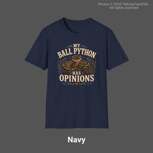 Pu&ograve; includere: Una t-shirt blu navy a maniche corte con una grafica raffigurante un pitone reale avvolto circondato da fogliame. Il testo MY BALL PYTHON HAS OPINIONS &egrave; scritto in color crema, con piccoli cuori decorativi e ghirigori ornamentali.