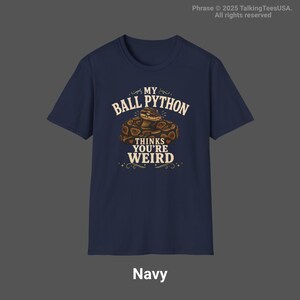 May include: A navy blue short-sleeve t-shirt featuring a graphic of a coiled ball python snake. The text printed in cream-colored lettering reads: MY BALL PYTHON THINKS YOU'RE WEIRD. The design includes decorative flourishes and small heart accents.