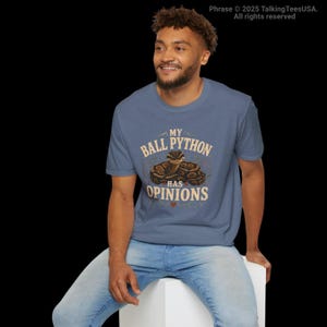 Pu&ograve; includere: Una t-shirt a maniche corte blu m&eacute;lange con la grafica di un pitone reale avvolto. Il testo "MY BALL PYTHON HAS OPINIONS" &egrave; stampato in beige, con una piccola icona a forma di cuore rosso sotto l'illustrazione del serpente sul petto.