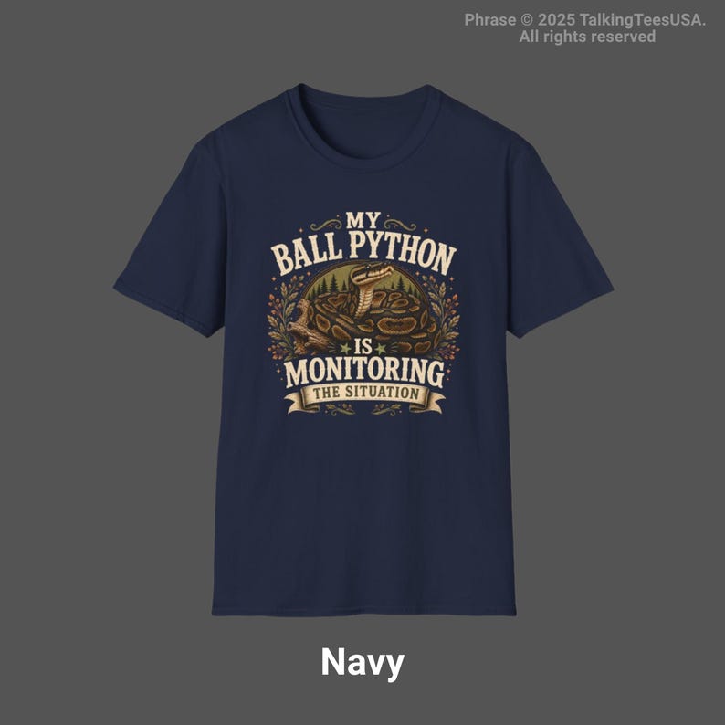 Puede incluir: Una camiseta de manga corta azul marino con un gr&aacute;fico de una pit&oacute;n bola enroscada en una rama. El texto dice MY BALL PYTHON IS MONITORING THE SITUATION, rodeado de follaje decorativo y un dise&ntilde;o de pancarta en tonos tierra.