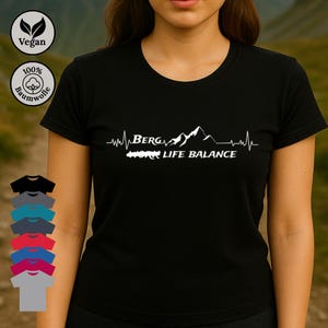 Könnte beinhalten: Schwarzes T-Shirt mit Rundhalsausschnitt und weißem Grafikdesign. Das Design enthält das Wort "BERG", eine Bergkette und die Worte "LIFE BALANCE". Das Shirt hat auch vegane und Baumwollsymbole.