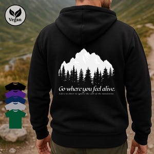 Peut inclure: Sweat à capuche noir avec un motif de montagne et de forêt blanc au dos. Le texte "Go where you feel alive" et "Life's to short to ignore the call of the mountains" sont en dessous. Un logo végétalien est dans le coin supérieur gauche.