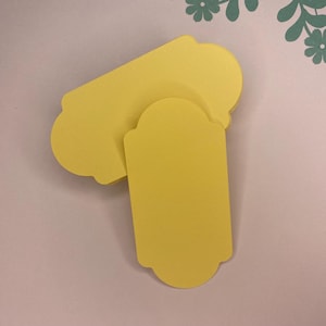 May include: Two yellow paper gift tags with scalloped edges. The tags are blank and ready to be written on.