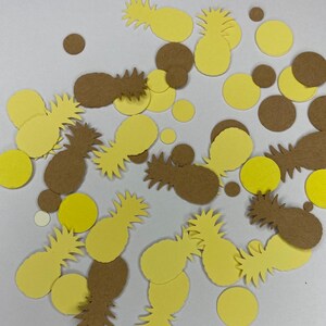May include: Overhead shot of scattered yellow and brown paper cutouts. The cutouts include pineapple shapes and circular shapes. The pineapples are in various shades of yellow and brown. The circles are yellow and brown.