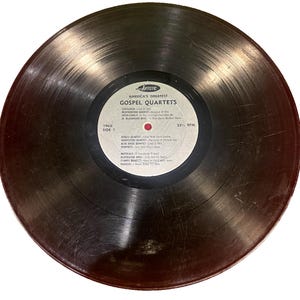 Puede incluir: Un disco de vinilo negro con una etiqueta blanca. La etiqueta tiene el texto "America's Greatest Gospel Quartets" y enumera las canciones del disco. El disco es de 1965 y gira a 33 1/3 RPM.