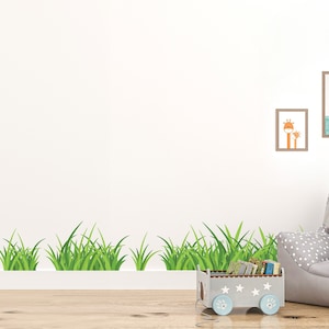 以下が含まれることがあります： 白い壁の下部に緑の草の縁取りがあります。壁には、キリンとラマの絵が描かれた額縁が2つあります。画像の右下には、白い水玉模様の灰色の猫の形をした椅子があります。椅子の前には、白い星がついた青いおもちゃのワゴンがあります。