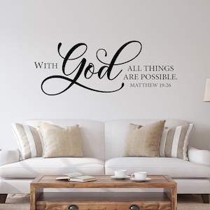 May include: White couch with pillows in a living room setting. A wooden coffee table with two mugs on it. A wall decal with the text "With God all things are possible. Matthew 19:26"