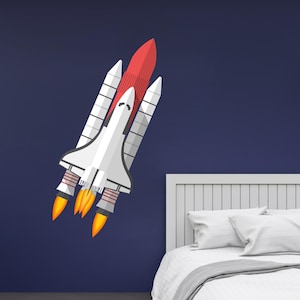 Puede incluir: Una lanzadera espacial blanca y roja con tres llamas naranjas que salen de la parte inferior del cohete. La lanzadera está en una pared azul oscuro con una cabecera blanca detrás.