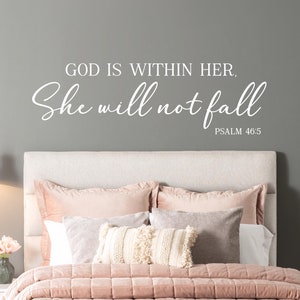 Puede incluir: Una calcomanía de pared blanca con el texto "Dios está en ella, no caerá, Salmo 46:5" sobre una cama rosa con almohadas blancas y crema.