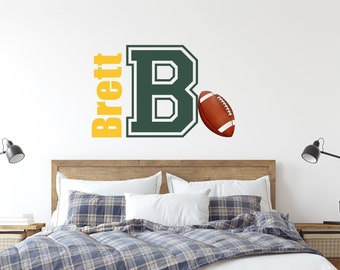Könnte beinhalten: Ein Schlafzimmer mit einem Holzbettgestell und einer blau-weißen karierten Bettdecke. Die Wand hinter dem Bett hat einen grünen und weißen Buchstaben "B" mit einem Fußball und den Namen "Brett" in gelben Buchstaben.