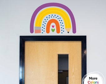 Puede incluir: Una calcomanía de pared de arcoíris púrpura, amarillo y naranja con un diseño de lápiz. El arcoíris está decorado con lunares azules y corazones rojos. El texto "Más colores disponibles" está en un círculo debajo del arcoíris.