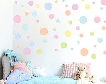Puede incluir: Una pared blanca con lunares de colores pastel de varios tamaños. La pared está detrás de una cama azul claro con una cabecera blanca y una almohada en forma de nube blanca.