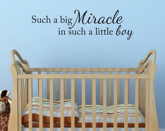 May include: A white cot with a striped blanket and a stuffed giraffe toy. The wall behind the cot has a black vinyl decal that reads "Such a big Miracle in such a little boy."