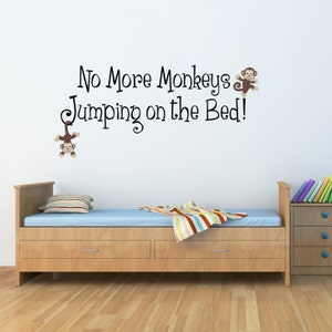 Peut inclure: Un mur blanc avec un autocollant en vinyle noir et brun qui dit "No More Monkeys Jumping on the Bed!" avec deux singes de dessin animé de chaque côté du texte. L'autocollant est au-dessus d'un lit en bois avec une couverture bleue et un jeté rayé.