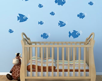 May include: A wooden crib with a white mattress and a blue wall with blue fish decals. A stuffed giraffe toy is sitting on the floor in front of the crib.