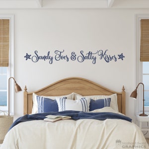 May include: A white bed with a wooden headboard and blue and white striped pillows. The wall behind the bed has a blue and white decal that says "Sandy Toes & Salty Kisses" with a starfish on each side.