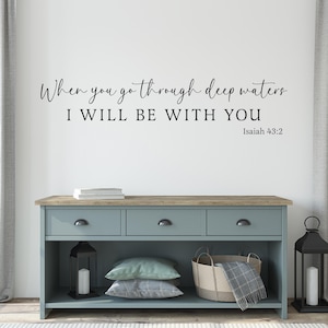 Puede incluir: Una calcomanía de pared con la cita "When you go through deep waters I WILL BE WITH YOU" y la referencia bíblica "Isaiah 43:2". La calcomanía se muestra en una pared blanca sobre una cómoda azul claro con tres cajones y un estante.