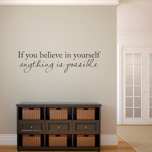 May include: A wall decal with the inspirational quote "If you believe in yourself anything is possible" in a black cursive font. The decal is placed on a light beige wall above a black dresser with six wicker baskets.