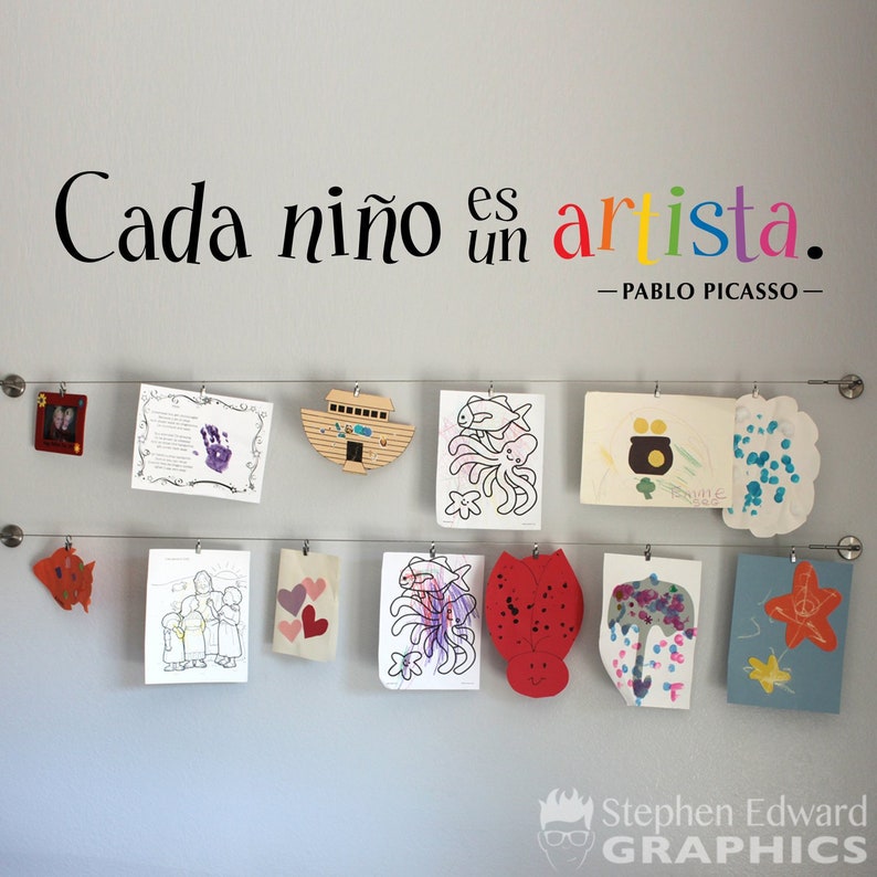 May include: A wall display of children's artwork, featuring colorful drawings and paintings, with the quote "Cada ni&ntilde;o es un artista." - Pablo Picasso.