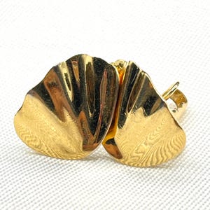 May include: A pair of gold-toned metal earrings featuring a polished, fan-like shell design with vertical ridges. The earrings have a smooth, reflective surface and a curved, organic shape that mimics the appearance of a natural fan shell.