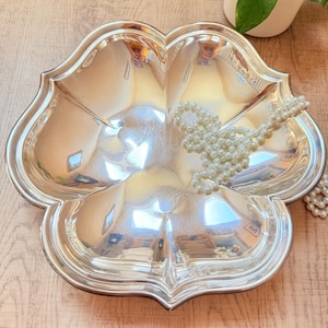 May include: A silver-colored, three-sectioned serving dish with a scalloped edge. A strand of white pearls rests on the dish. The dish is on a wooden surface.