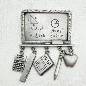 May include: A silver-toned brooch shaped like a chalkboard with math formulas and a circle. Dangling below are a calculator, ruler, book with "MATH" on it, pencil, and an apple. The brooch is a school-themed accessory.